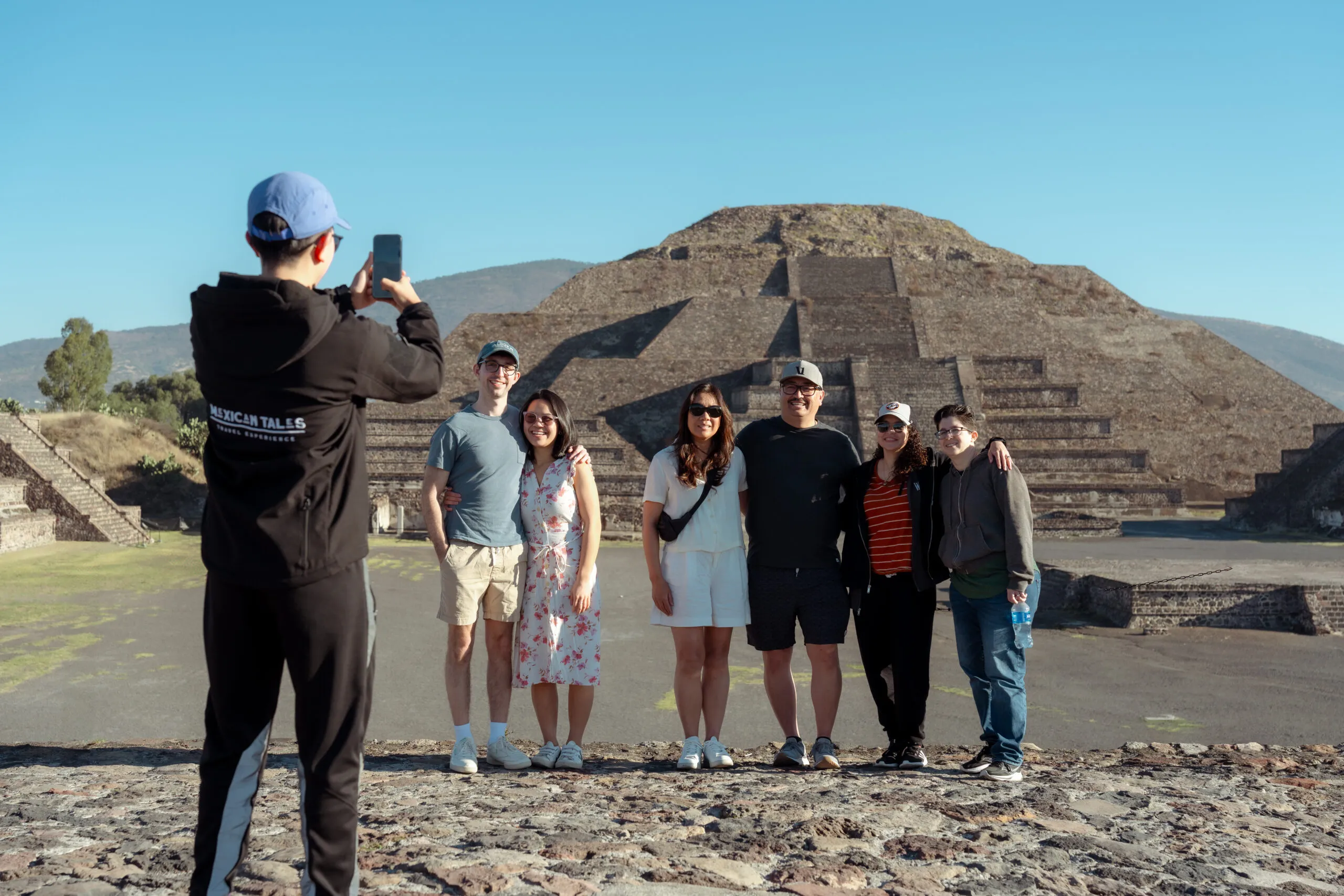 A friendly guide takes a group photo with the pyramid in the background. Experience the best Teotihuacan pyramids tour.