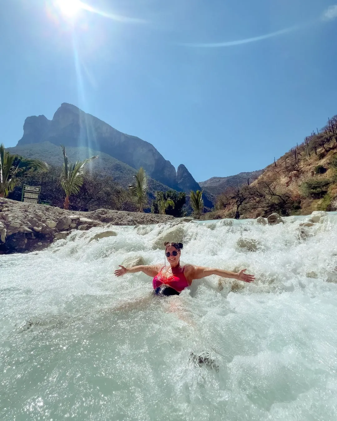 : Feel the thrill of Tolantongo tours in the thermal river. Woman smiling and floating in the canyon's turquoise waters.