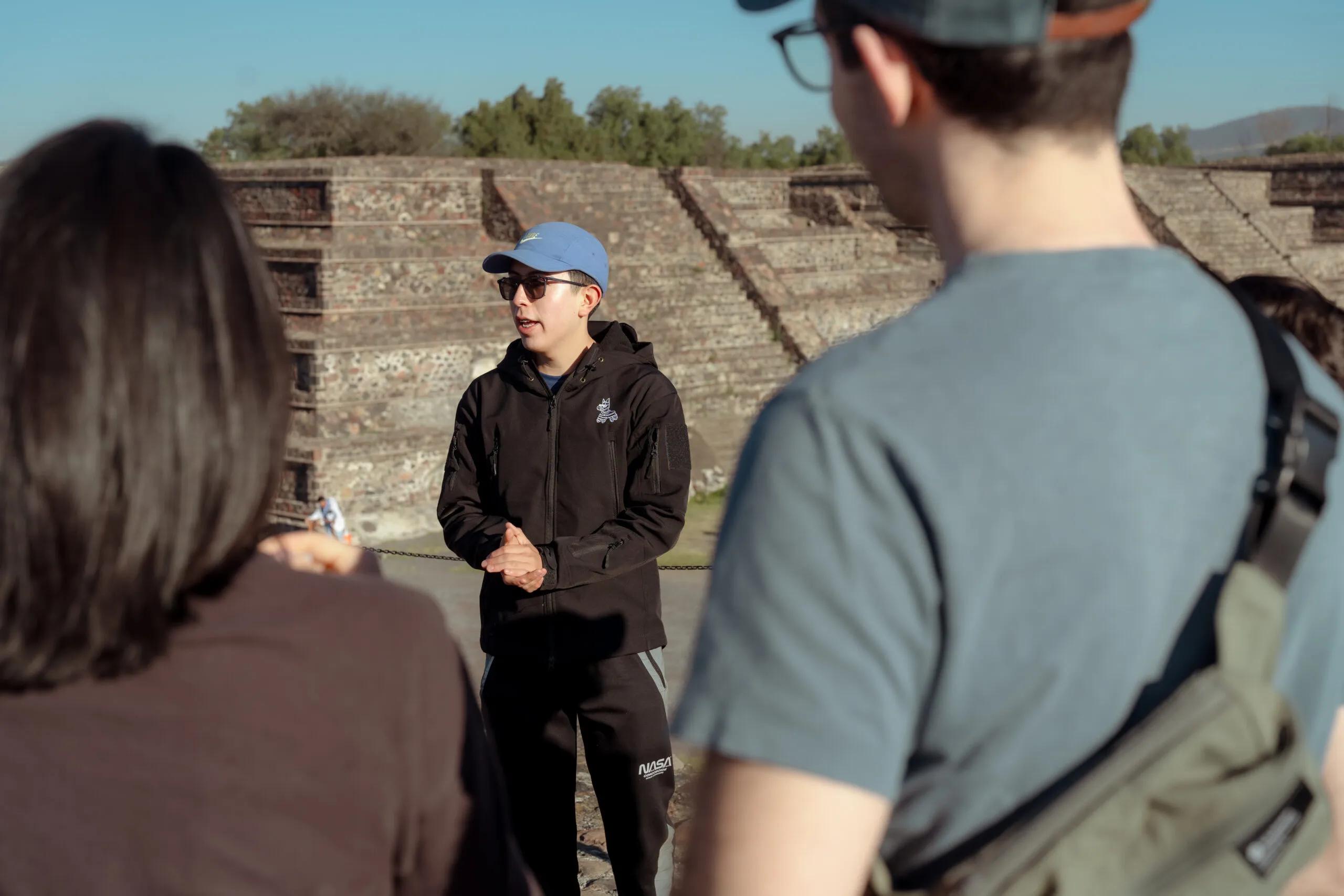 Expert guide in blue cap sharing history with tourists at the archeological site. Book your Teotihuacan pyramids tour now.