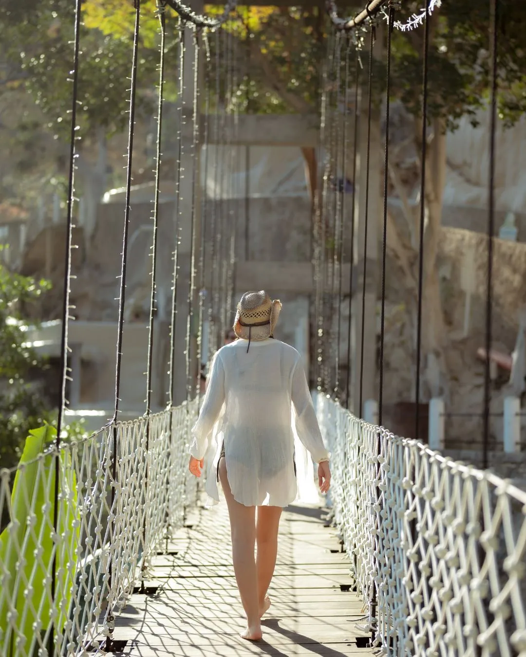 Embark on an adventure with Tolantongo tours: Woman walking towards lush nature, crossing a beautiful rope suspension bridge.