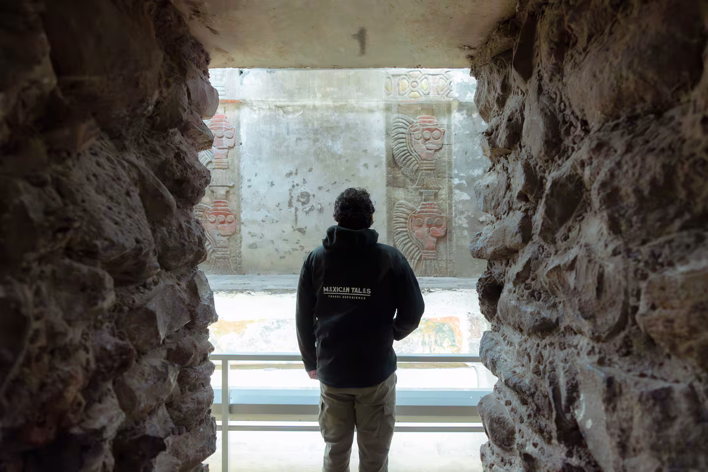 Visitor looking at ancient murals through a stone archway. Discover the mysteries on a Teotihuacan pyramids tour.