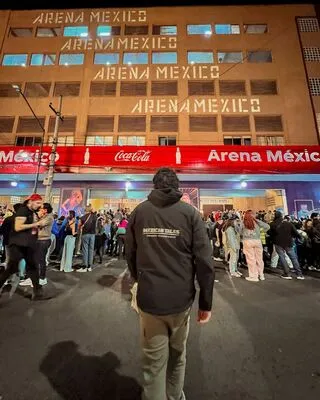 Back view of a person wearing a Mexican Tales jacket, looking at the iconic Arena México entrance, ready for the Lucha Libre show.