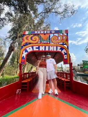 Couple posing at the bow of a trajinera decorated with "MEXICO XOCHIMILCO," partaking in a private Xochimilco tour.