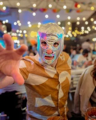 Excited tourist wearing a shimmering silver Lucha Libre mask, reaching out during a Mexican Tales tour dinner event.