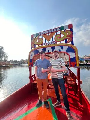 Two men enjoying drinks on a red trajinera under the sun on the water, a classic Xochimilco tour experience for tourists.