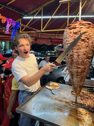 A happy young man carving al pastor meat. The best Mexican food to celebrate a World Cup victory after the final match.