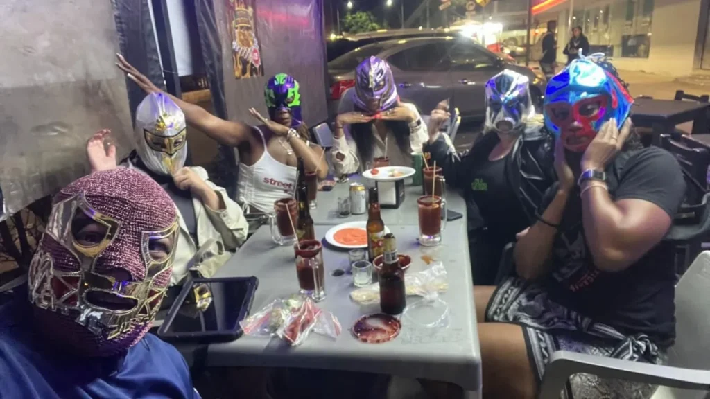 A large group of friends poses with Mexican wrestling masks and spicy beer drinks to show what is a michelada at night.