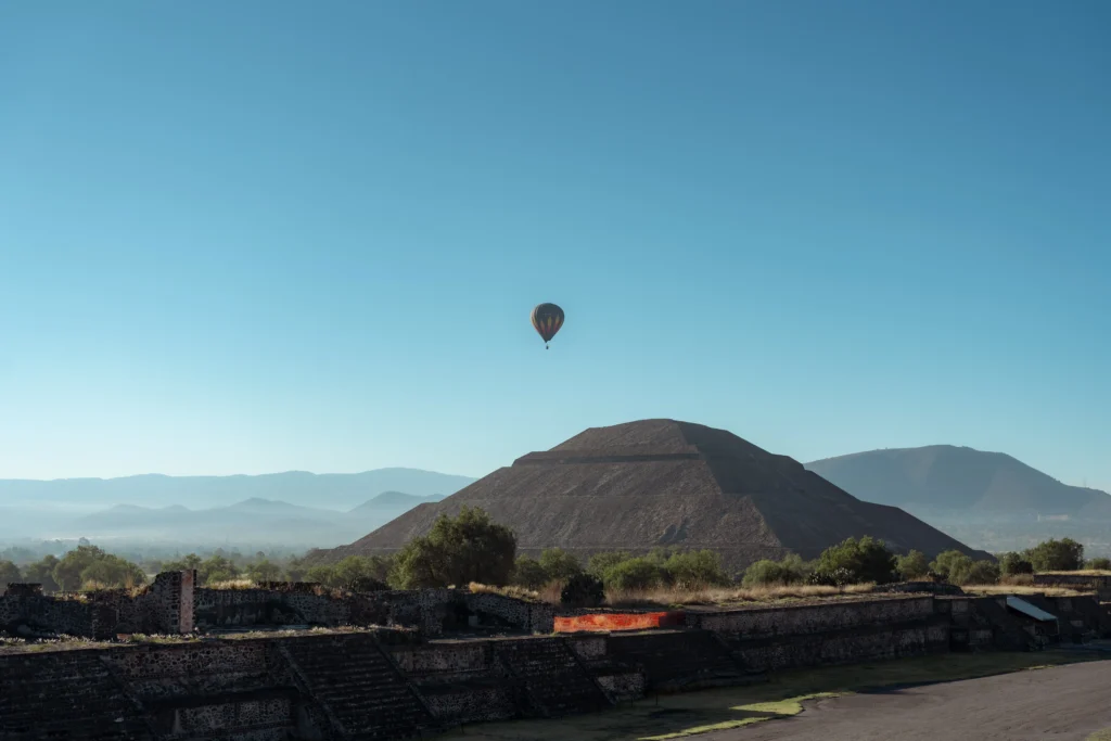 A colorful hot air balloon floating over the Sun Pyramid during a morning Teotihuacan Pyramids Tour in Mexico.