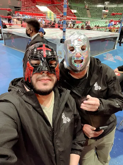 Two men posing by the ring side while wearing traditional wrestler masks at a Lucha Libre in Mexico City event.