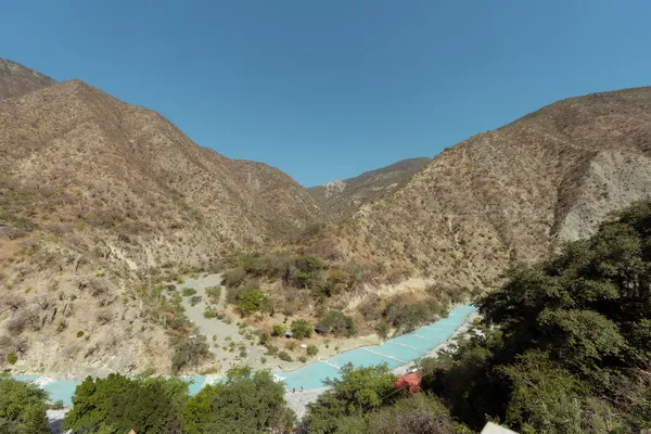 A high wide-angle view of a dry canyon valley with a bright turquoise river running through Cenotes and Hot Springs near Mexico City.
