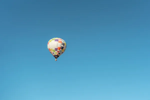 A colorful checkered hot air balloon high up in a clear blue sky during a fly in a hot air balloon over Teotihuacán experience.
