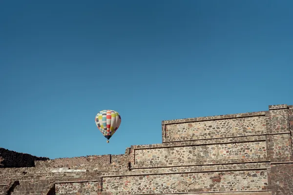 A vibrant hot air balloon floating near the stone pyramid walls during a sunrise hot air balloon ride over Teotihuacán.
