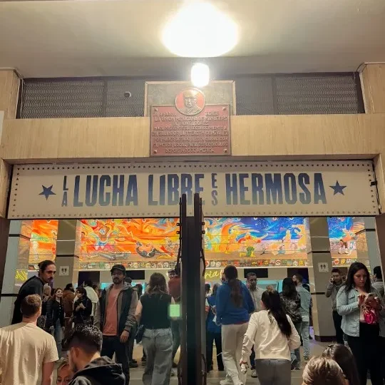 Fans walking under a sign reading 'LA LUCHA LIBRE ES HERMOSA' for Lucha Libre Mexico City.
